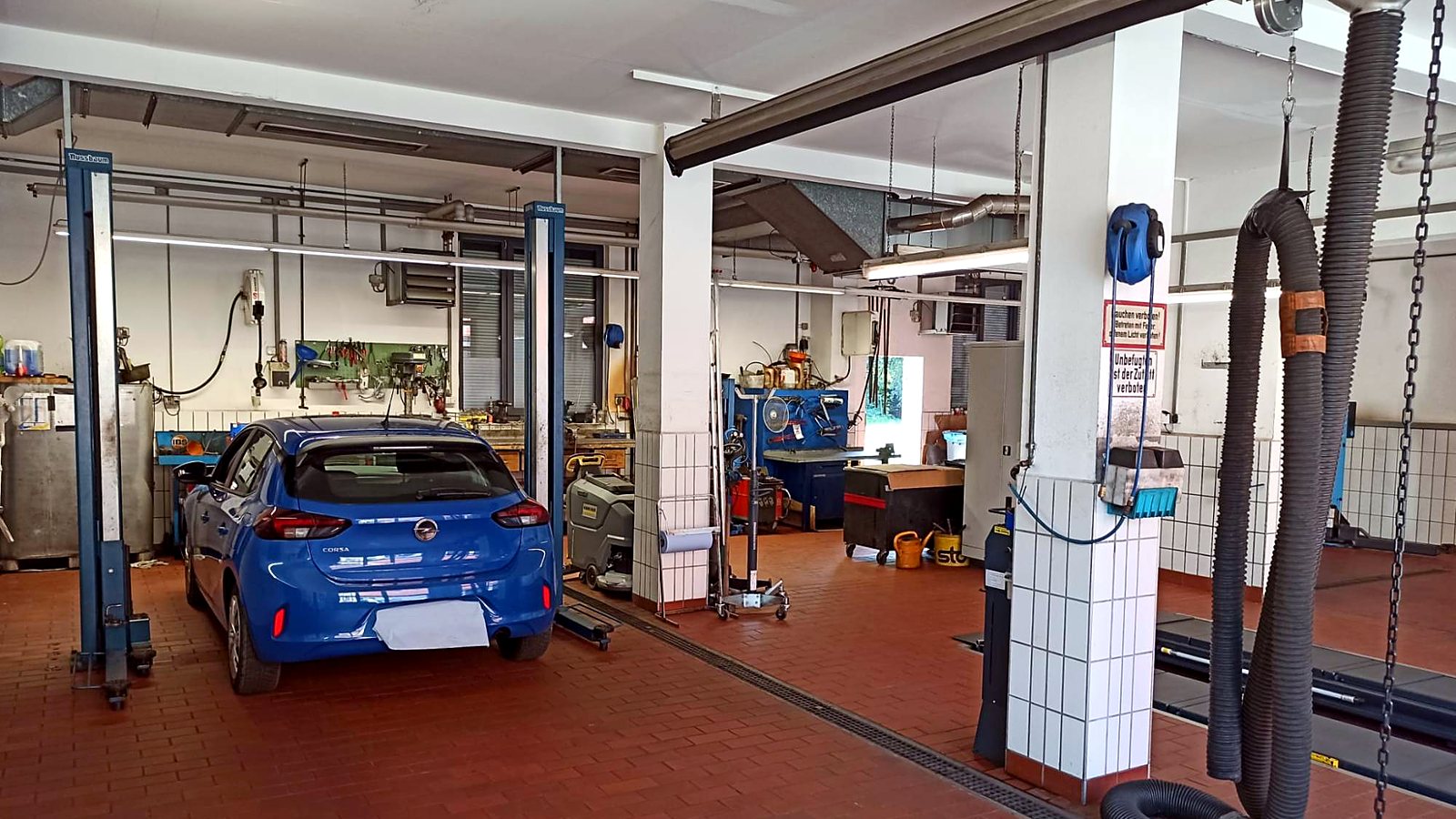 Werkstatthalle von Auto Scharrer mit blauem Opel Corsa an der Hebebühne, Werkbänken und Abgasabsaugung